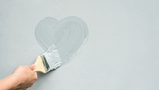 The hand of the master with a brush paints a heart on the wall.