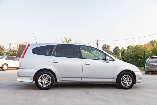 right side view of a honda stream car in a silver body japanese 2002 year van in a parking lot with a green trees and asphalt. - year 2002 imagens e fotografias de stock