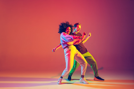 Hombre y mujer elegantes bailando hip-hop con ropa brillante sobre fondo degradado en el salón de baile con luz de neón photo