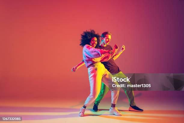 Stylish Man And Woman Dancing Hiphop In Bright Clothes On Gradient Background At Dance Hall In Neon Light Stock Photo - Download Image Now