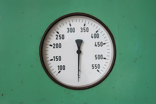 Round industrial thermometer on a machine green background