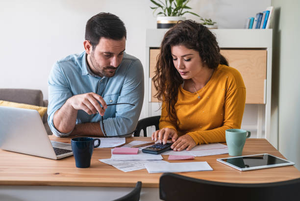 Young couple calculating their domestic bills at home stock photo Focused married couple manage finances, use internet banking service on computer and calculator at modern kitchen desk ipad calculator stock pictures, royalty-free photos & images