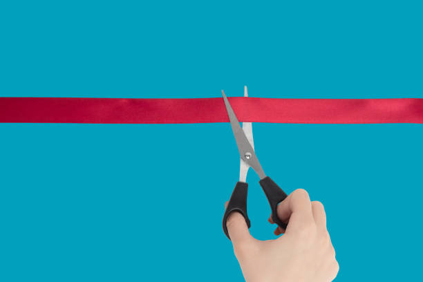 istock Female Hand scissors cuts a red ribbon. Isolate on a blue background. 1267344303