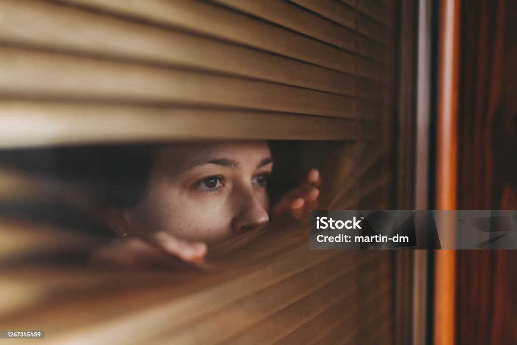 Lockdown during COVID-19 pandemic Woman at home during COVID-19 pandemic is looking through window Fear Stock Photo