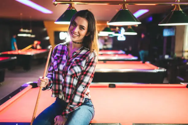 Young Caucasian beautiful woman sitting on pool table.