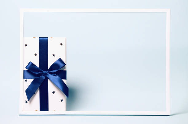 istock Present box  wrapped with blue ribbon on colorful background with white frame. Festive and holiday theme. Christmas or birthday gift. 1267365925