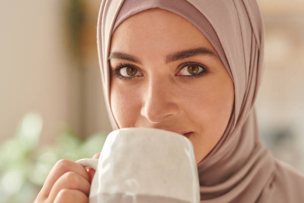 горизонтальный крупным планом портрет красивой ближневосточной женщины в хиджабе, пьющие чай, глядя в камеру - women middle eastern ethnicity islam hijab стоковые фото и изображения
