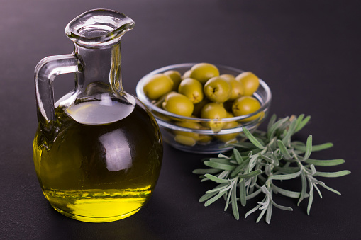 Olive oil in a decanter and a sprig of  rosemary on a black background.