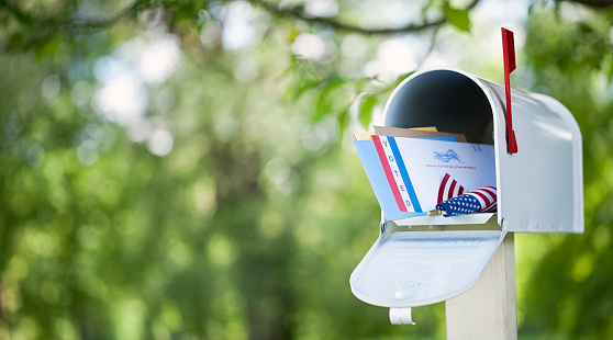 Voting by mail concept. Absentee ballot envelope in a mailbox against a defocused nature background.