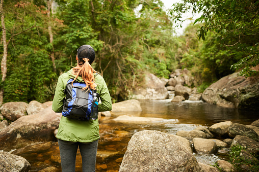 Rear view of a woman with backpack standing at mountain creek