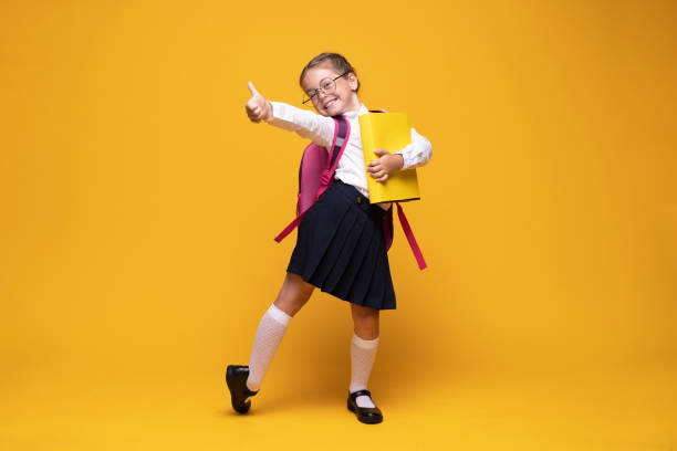 education, school, childhood, people and vision concept - smiling cute little girl with black eyeglasses showing thumbs up gesture over yellow education, school, childhood, people and vision concept - smiling cute little girl with black eyeglasses showing thumbs up gesture over yellow background school uniform stock pictures, royalty-free photos & images