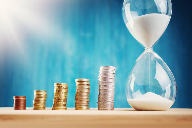 istock clock with stacked coins and hourglass on blue background 1267383409