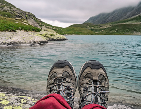 Person in trekking boots relaxing at lake or river water background