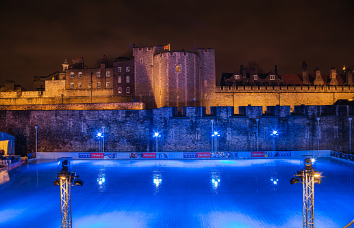 Empty and illuminated blue lights of The Tower of London ice rink after sunset on Christmas holiday in The Tower Hill, London, England