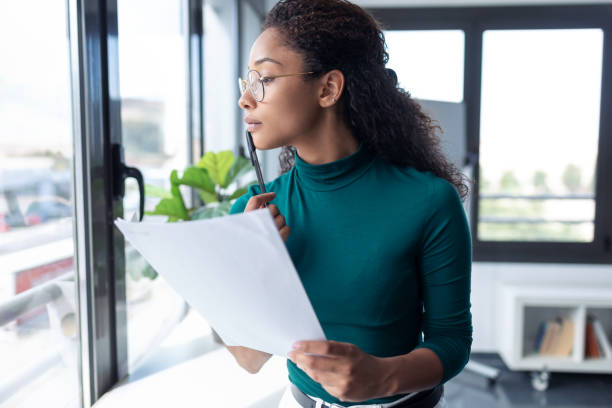 istock Concentrated young woman reading some documents while looking through the window in the office. 1267387032