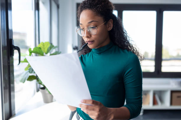 istock Concentrated young woman reading some documents standing next to the window in the office. 1267387174