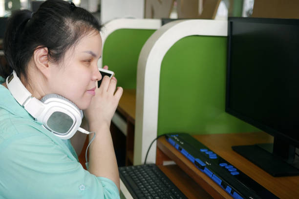 asiatisk ung blind person kvinna med hörlurar med hjälp av smart telefon med röst hjälpmedel för funktionshinder personer på arbetsplatsen med dator och punktskrift display på bordet. - tillgänglighet blind braille bildbanksfoton och bilder
