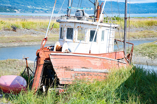 An aged boat rests on sandy shores, revealing its deck and engine