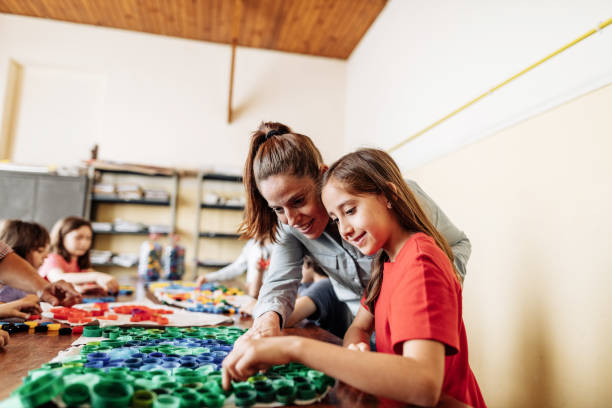 istock Elementary school teacher assisting school girl in making crafty work 1267395790