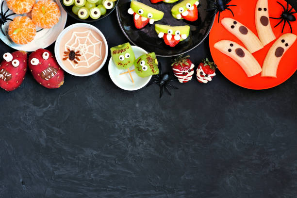 istock Healthy Halloween fruit snacks. Overhead view top border over a black stone background. 1267397026