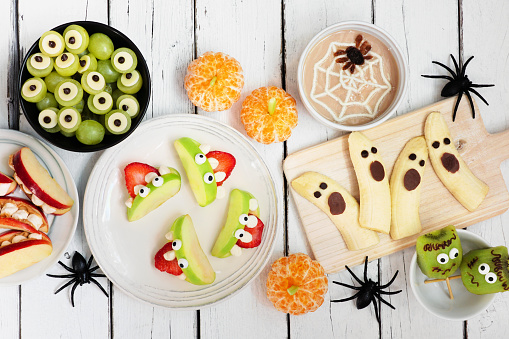 Healthy Halloween fruit snacks. Variety of fun, spooky treats. Top view table scene over a white wood background.