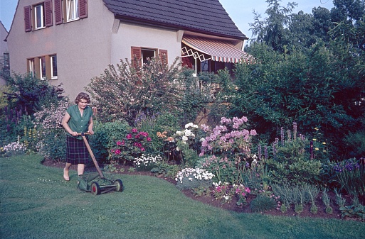 Erlangen, Middle Franconia, Bavaria, Germany, 1969. A woman cuts the lawn of her garden with a cylinder mower.
