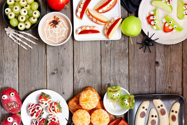 Healthy Halloween fruit snacks. Above view double border over a rustic wood background.