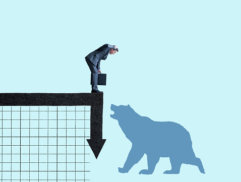 A businessman looks down at the impending onset of a bear market isolated on a light blue background.