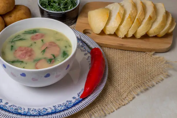 Caldo Verde Soup is a popular soup in Portuguese cuisine with greens and chopped chorizo on the top in ceramic bowl and piece of bread and pepper. Top View