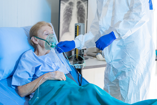 Medical team giving oxygen mask to the elderly covid-19 patient in quarantine room. Caucasian woman are suffering from a lung infection in restricted areas. Part of coronavirus 2019-2020 global pandemic