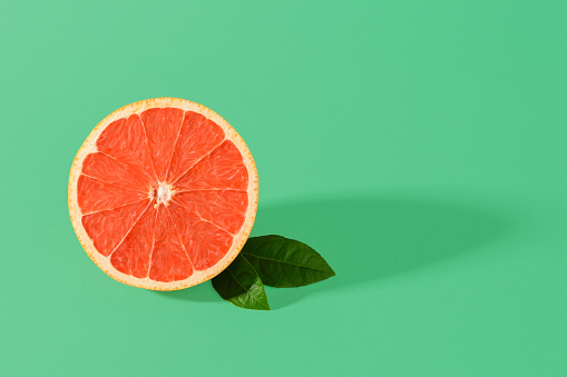 Half of ripe juicy pink grapefruit and two leaves with shadow on a green background. Organic antioxidant. Vegetarian, raw food diet and healthy eating. Copy space.