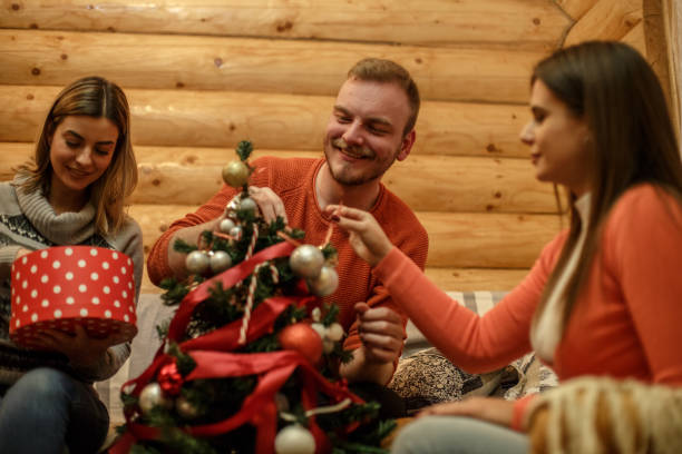 istock Three cheerful friends decorating a small Christmas tree 1267417281
