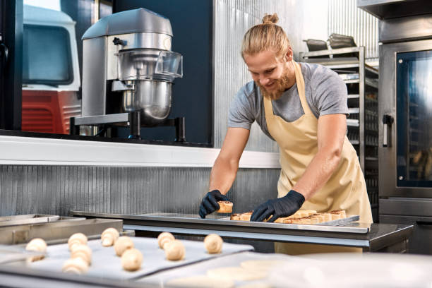 istock Small Business.Bearded man standing at bakery shop arranging cinnamon rolls on tray smiling playful and inspired 1267417362