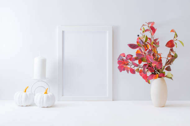 istock Home interior with decor elements. Mockup with a white frame, colorful autumn leaves in a vase on a light background 1267418181