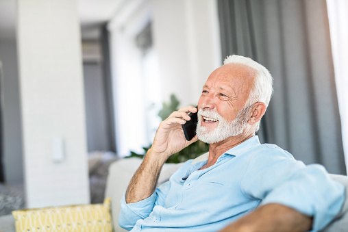 Senior man talking on phone and laughing in the living room of his home.