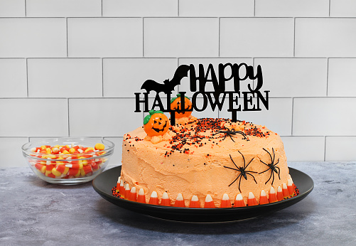 An orange frosted cake decorated for Halloween with a Happy Halloween banner, pumpkins, candy corn and spiders.