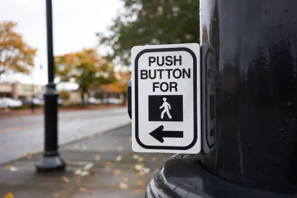 Push button for walk signal sign attached to a post on a city street.