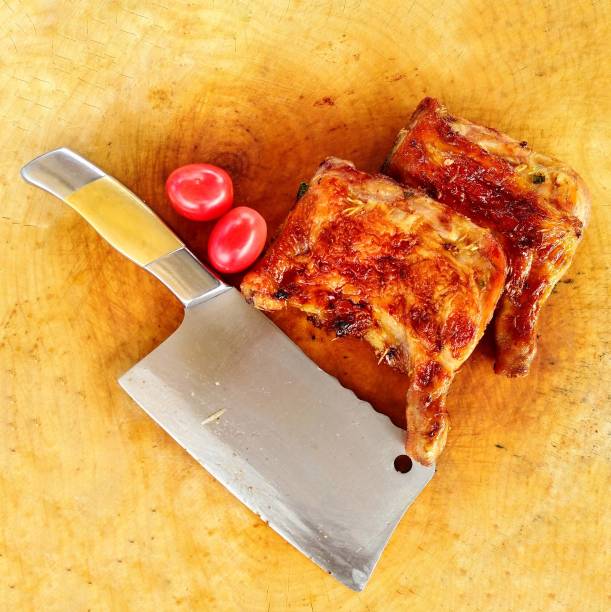 Preparing​ grilled chicken and tomato with kitchen knife on wooden butcher. Top view from above