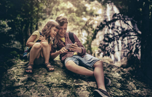 istock Two kids using smart phone sitting on a big rock in the forest 1267447771