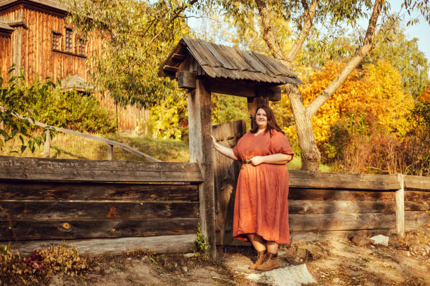 istock Beautiful and confident plus size model in red dress and brown boots  posing outdoors at autumn landscape with traditional russian architecture 1267456521