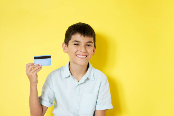 smiling little boy holding a credit card - paying children only retail childhood imagens e fotografias de stock