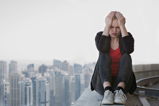 joven mujer de negocios estresada sentada en el borde de un rascacielos. tristeza y depresión. - suicide skyscraper anxiety at the edge of fotografías e imágenes de stock