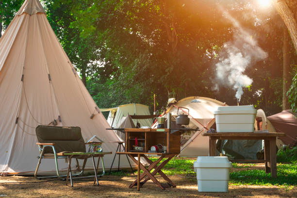 自然公園のキャンプ場にフィールドテントグループを備えた屋外キッチン機器と木製テーブルセット - テント 写真 ストックフォトと画像