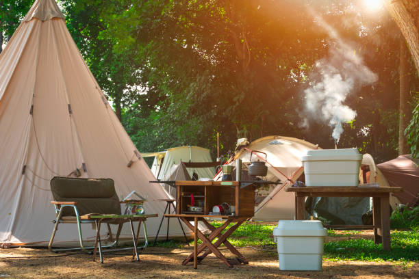 outdoor kitchen equipment and wooden table set with field tents group in camping area at natural parkland - acampando imagens e fotografias de stock