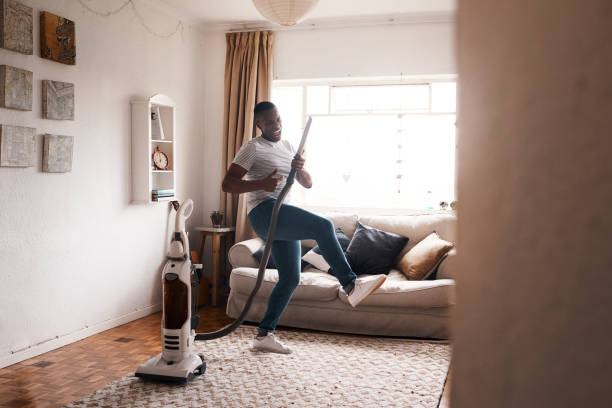 The vacuum is my favorite instrument Shot of a young man dancing while busy vacuuming the living room house cleaning stock pictures, royalty-free photos & images