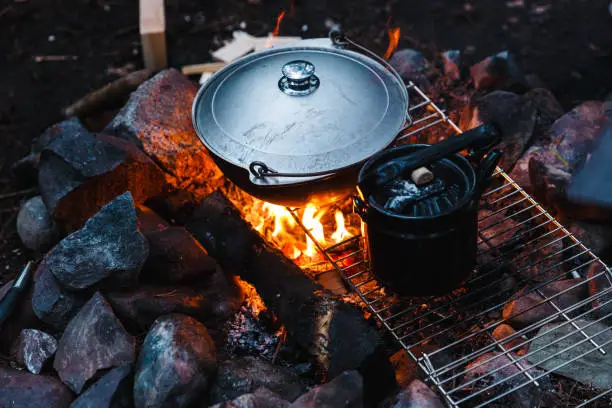 Photo of Summer outdoor rest. Camping in the forest in mountains. Cauldron and teapot on campfire. Cooking camp food