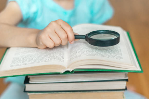istock A person (child) looks at a book through a magnifying glass (loupe). A stack of books on a blurred light background. Back to school. Education. Free time for the child. Love for reading. 1267463759