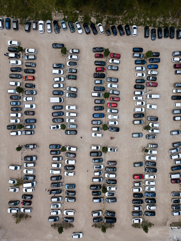 Aerial top down view of parking, many cars standing in row. Parked automobiles, trees. Parking on sand.