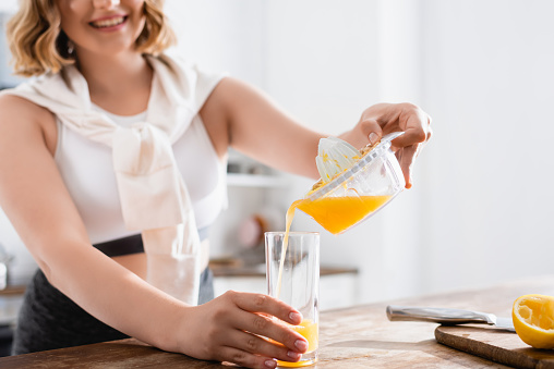 cropped view of woman pouring fresh orange juice in glass