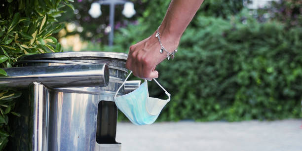 istock woman hand with utilized medical facemask near trash bin outside 1267470036